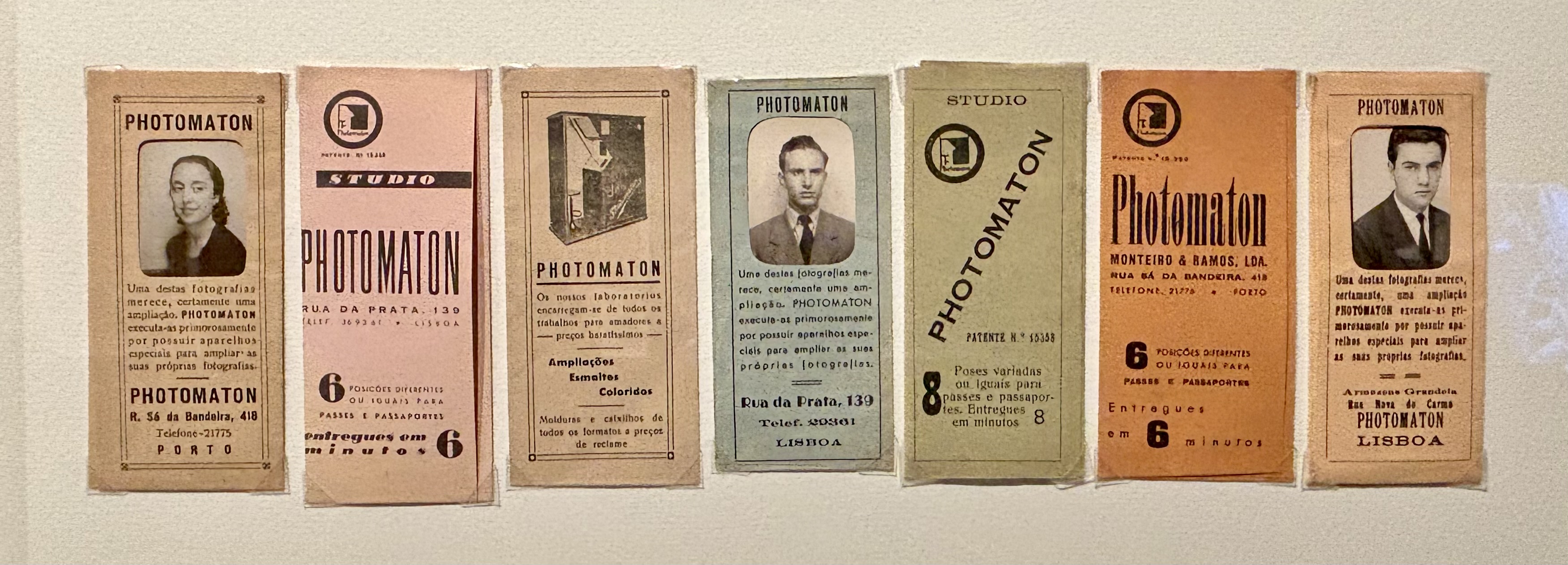 A row of six vintage Portuguese Photomaton photobooth tickets displayed on a wall, each with a portrait photograph and printed text. The tickets vary slightly in size, colour, and typography, ranging from beige, pink, green to brown tones. Each card advertises photobooth services, showing formal black-and-white headshots of men and women in mid-20th-century attire. The designs feature decorative borders, studio addresses in Porto and Lisbon, and information about photo enlargements, passport photos, and rapid processing times. 