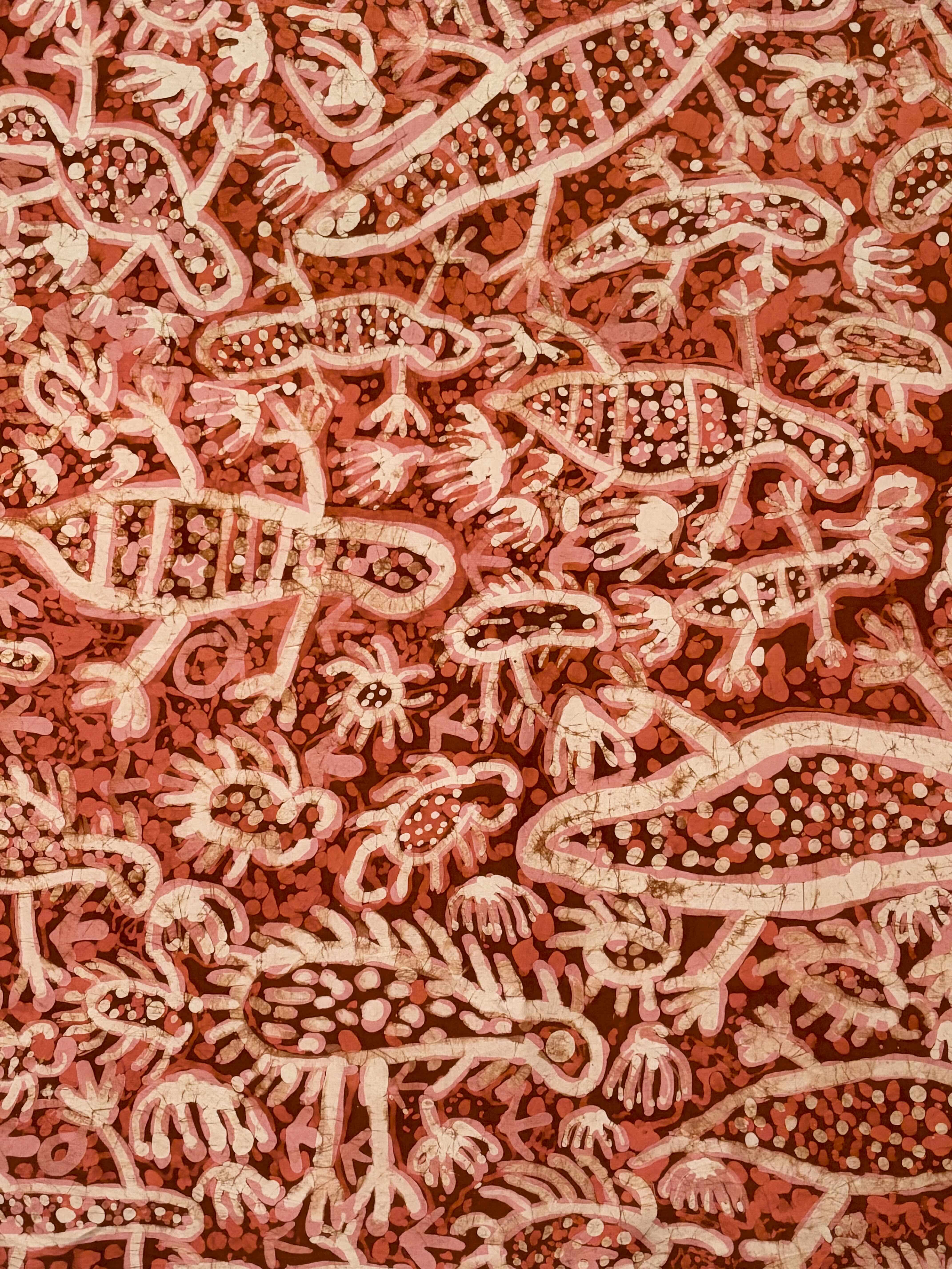 Batik on silk by Emily Kam Kngwarray (c. 1981) showing stylised arlewatyerr (sand goannas), ankerr (emus), small insects, and their tracks, rendered in pale pink and white forms over a dense red and ochre patterned background.
